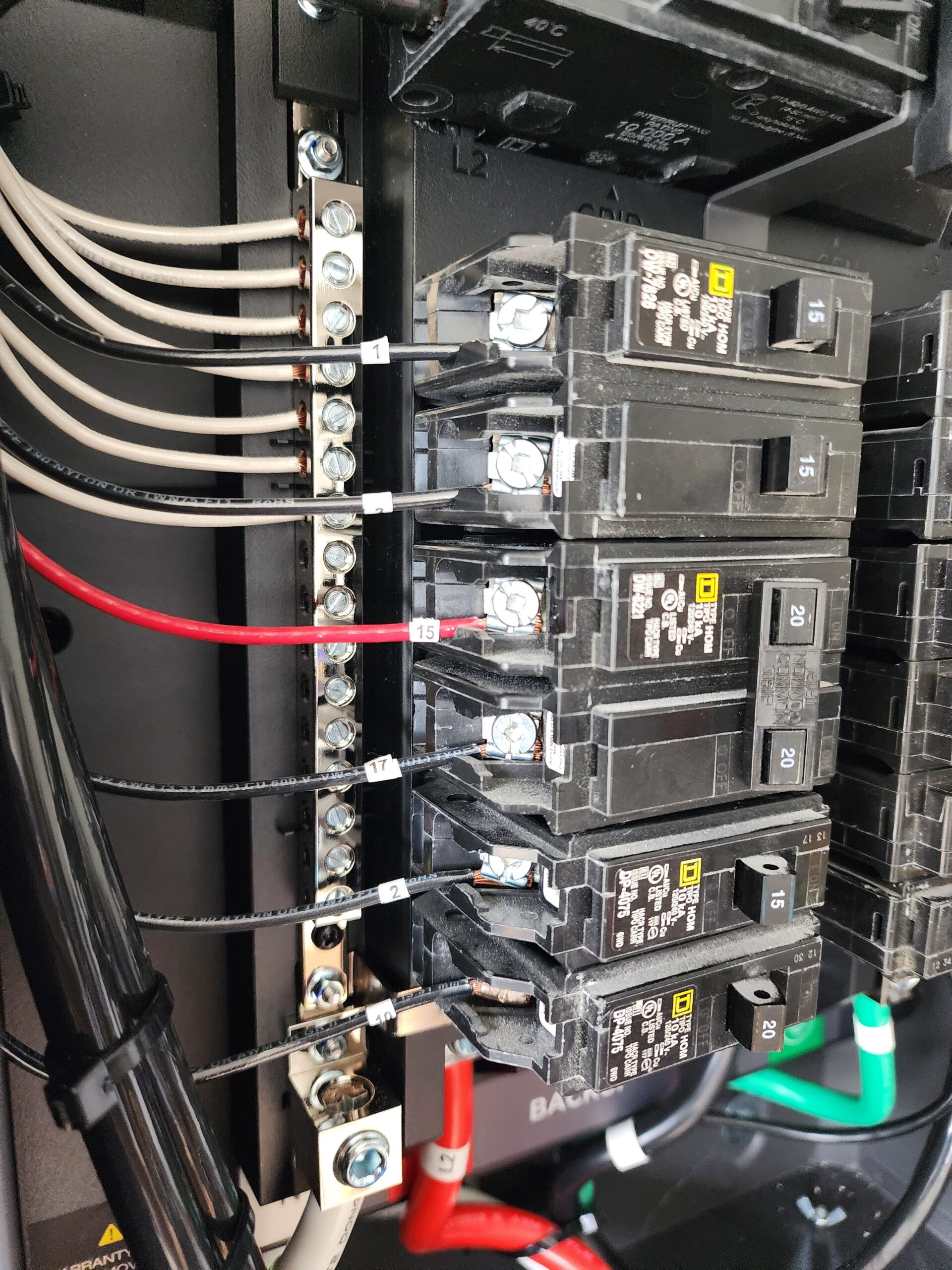 Close-up view of an electrical breaker panel showing multiple circuit breakers, wiring connections, and labeled wires.
