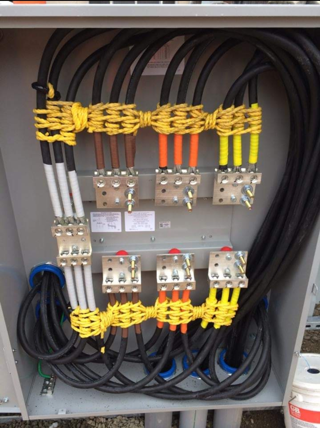 Electrical panel with organized cables secured by yellow rope, connected to metal terminals marked with colored insulation for identification.